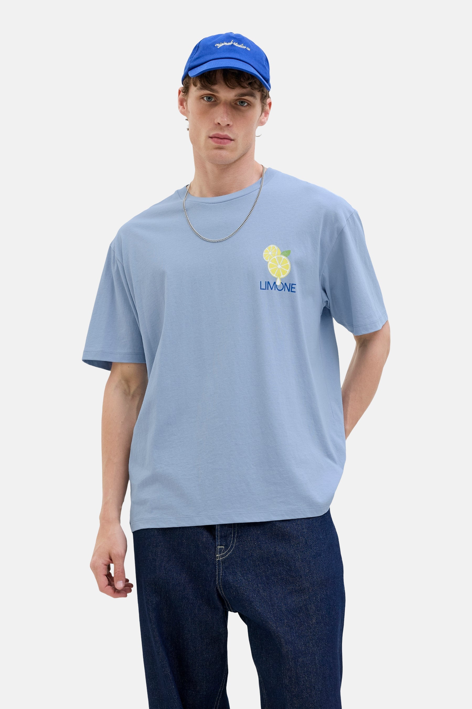 T-shirt bleu à manches courtes d'Originals by Jack & Jones, avec imprimé citron, porté avec des jeans bleus marine et un chapeau.