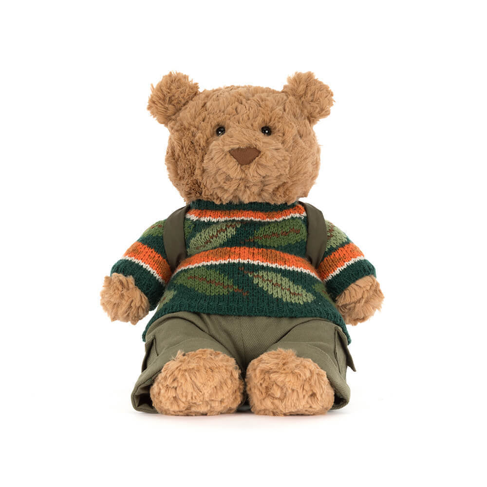 Stuffed teddy bear wearing a colorful sweater and green pants  with green back pack on a white background.