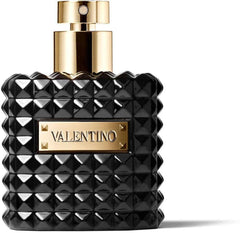 A black, square women’s perfume bottle by Valentino Perfumes with a studded texture and gold spray nozzle. The front bears a gold plate engraved “Valentino Donna Noir Absolu 3.4 EDP.” Set against a plain white background.