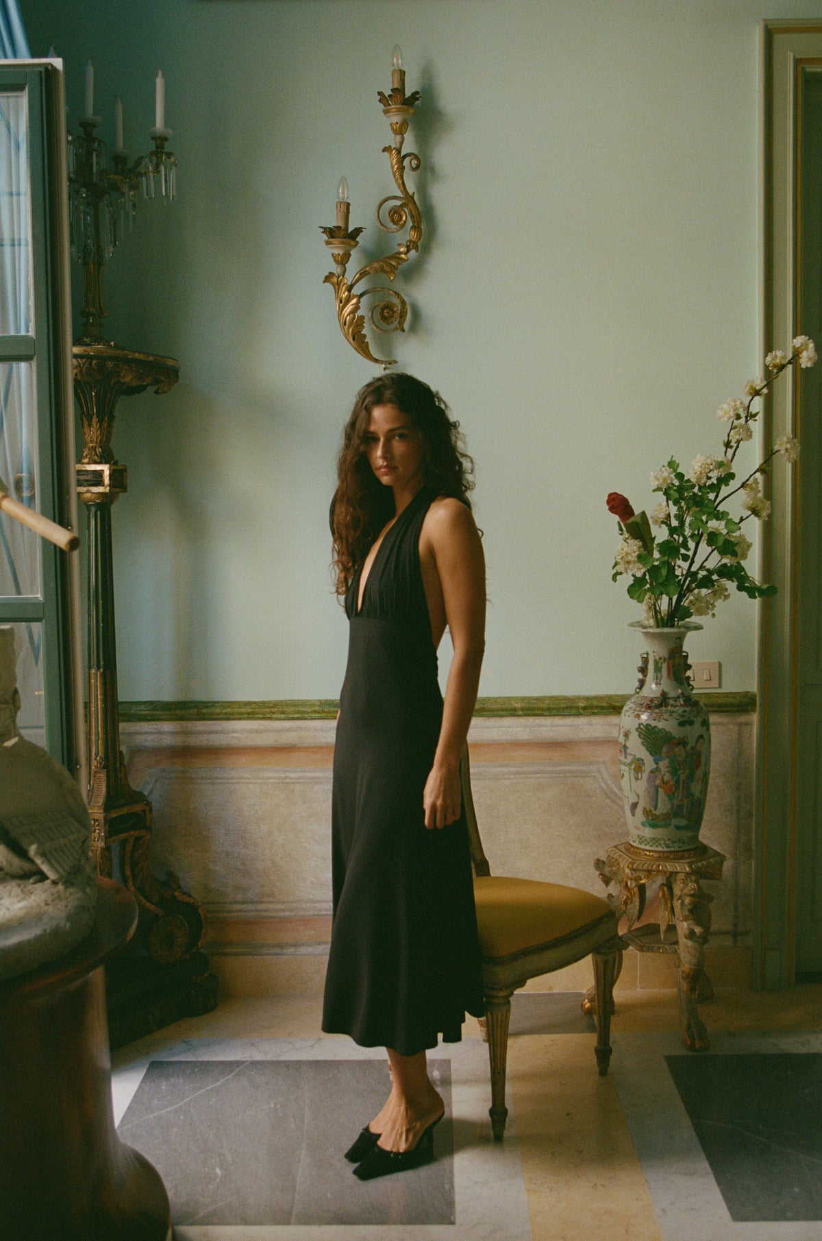 Woman in a black Jenavive midi halter neck dress with a low back, standing indoors.